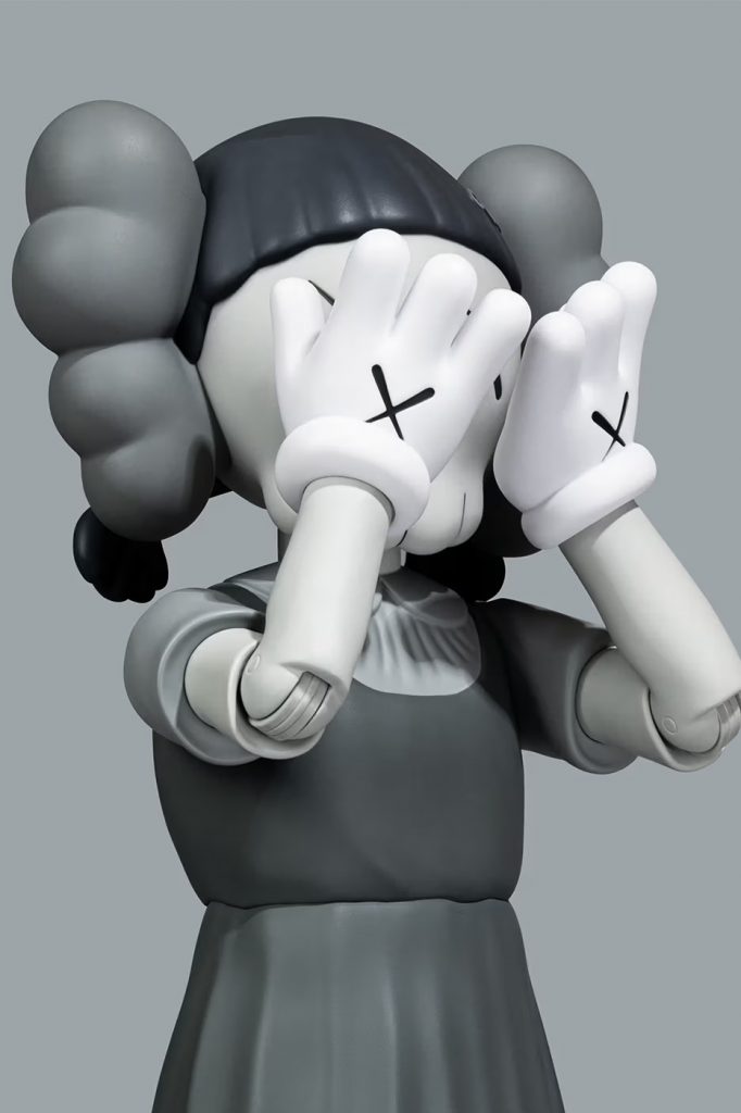 KAWS cartoon figurine with hands held up to its eyes to reveal two Xs on its hands