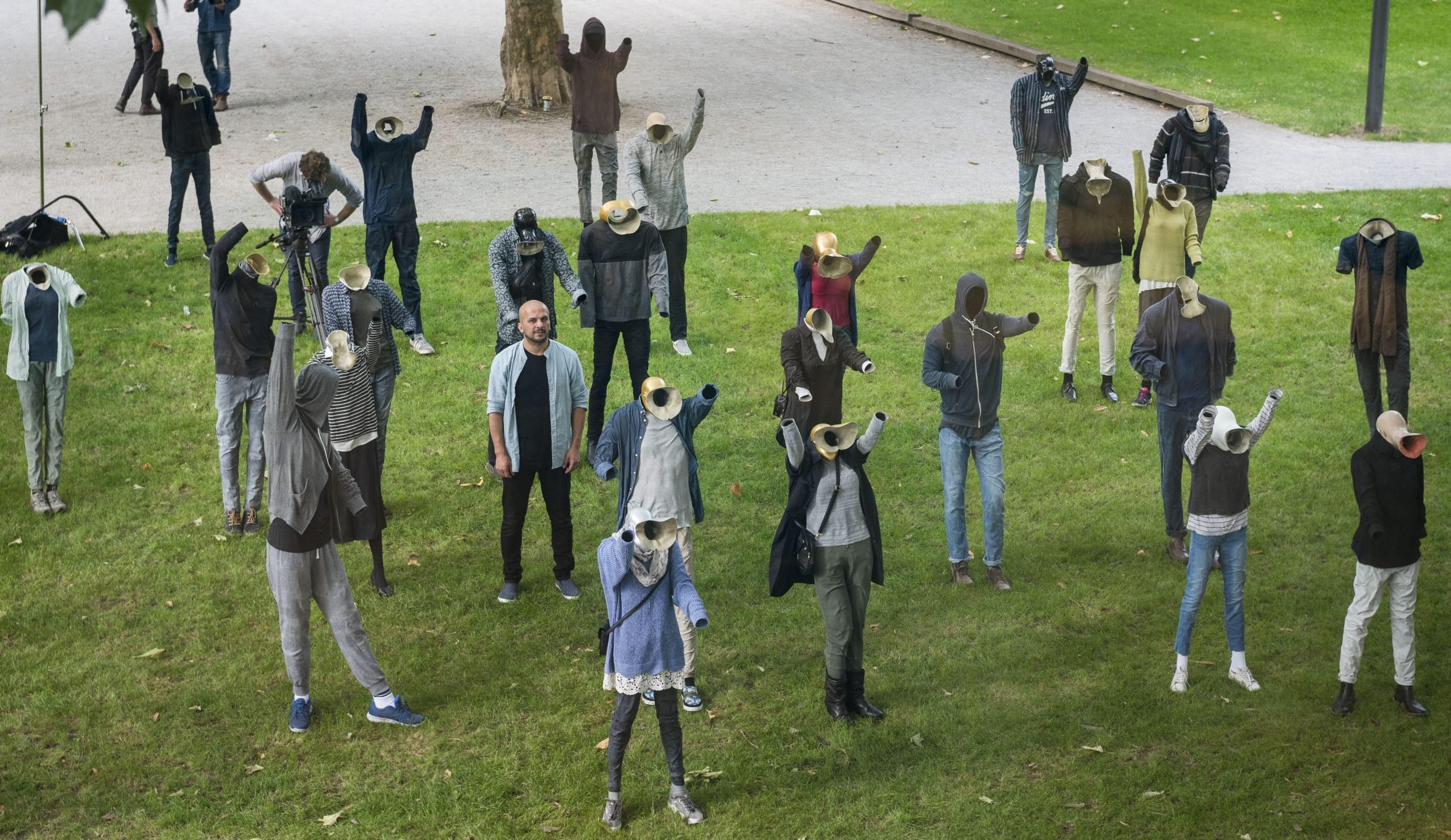 Artist Khaled Barakeh stands in an artwork consisting of human figures, no faces visible, standing outdoors, making protest gestures