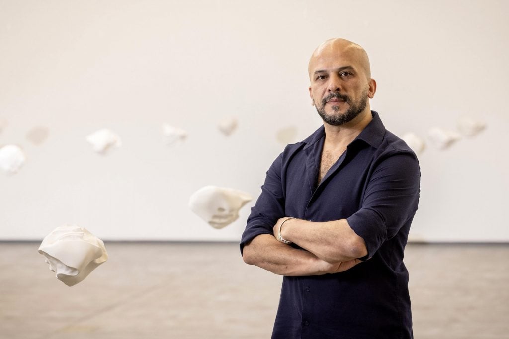 Syrian artist Khaled Barakeh stands with one of his artworks, with small sculptures hanging from the ceiling