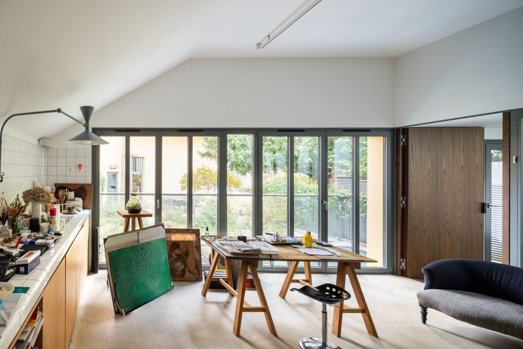 A photograph of a simple former artist studio, predominantly decked out in white, with one wall of paneled windows.