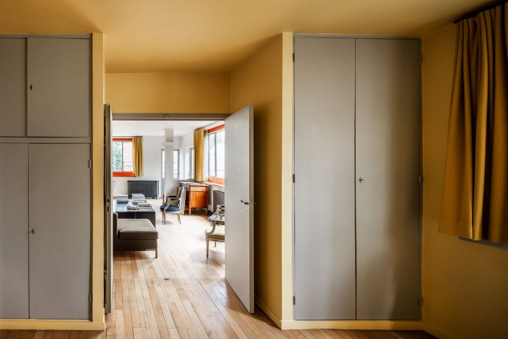 A photograph depicting the yellow bedroom within the Miestchaninoff House-Studio, leading out into the white lounge room before it.