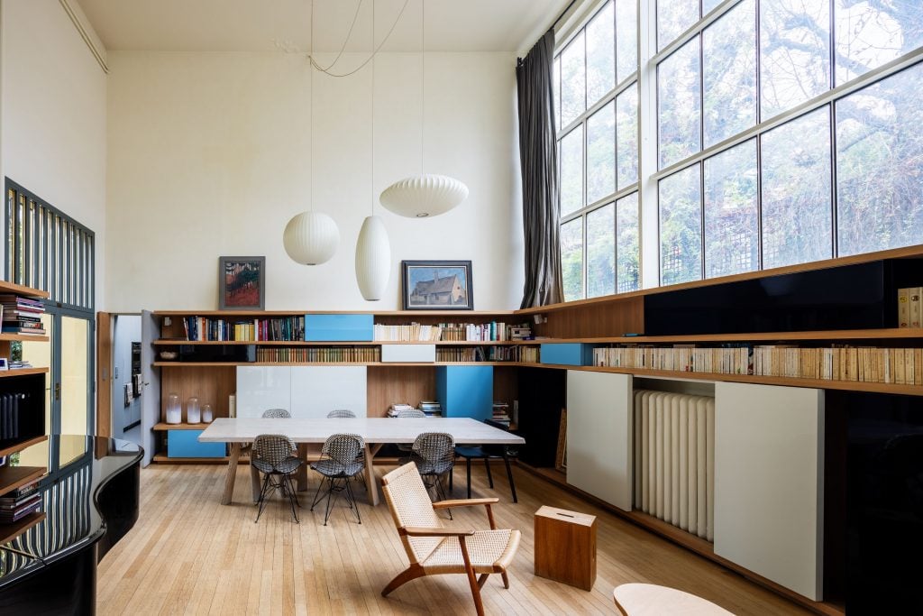 A photograph of an airy living room with a large bank of windows on its right wall.