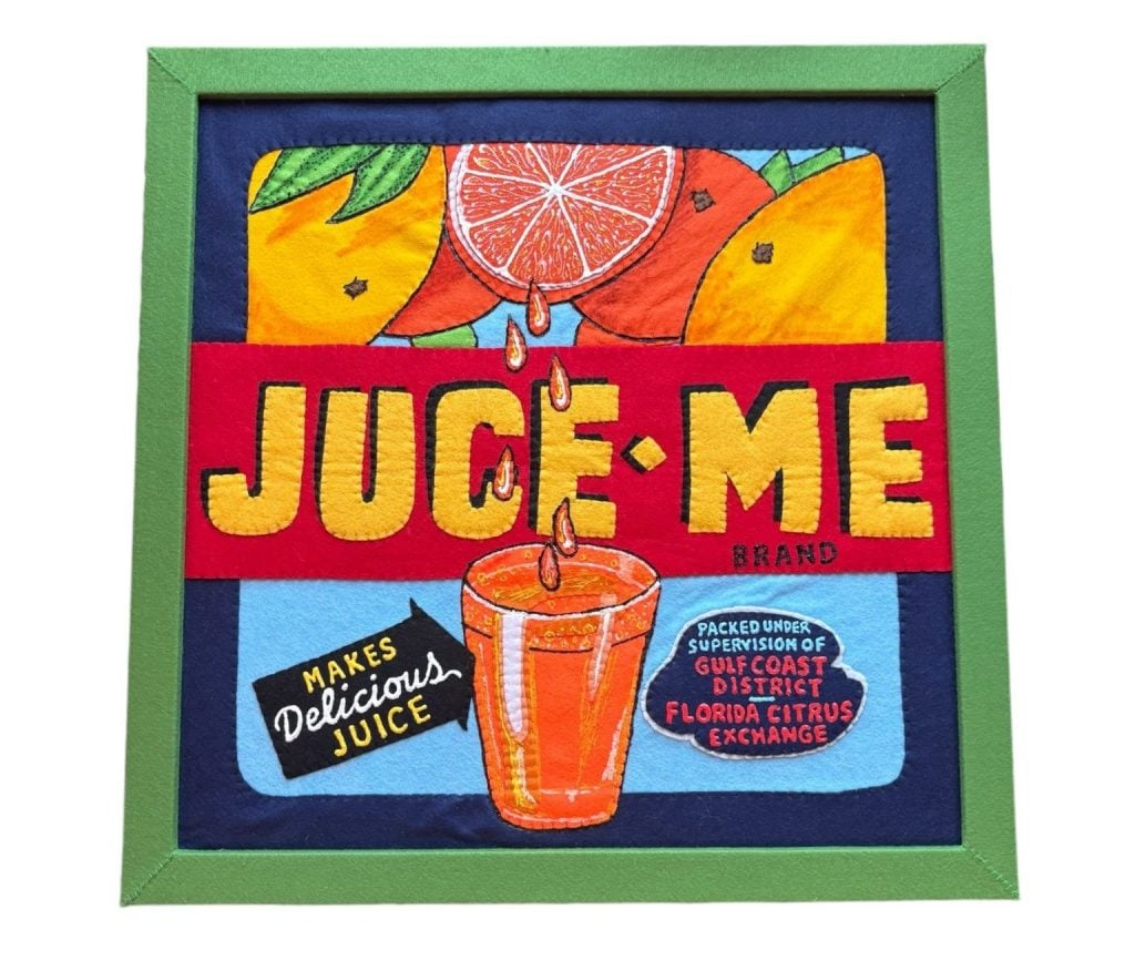 A felted Lucy Sparrow "painting" recreating a vintage ad for Florida orange juice with oranges, one cut open and squeezing out juice, on top the brand name "JUCE-ME" in yellow letters on a red stripe in the center, and a full glass on juice on a blue background, with advertising text on the sides. There is a blue border and a green frame. 