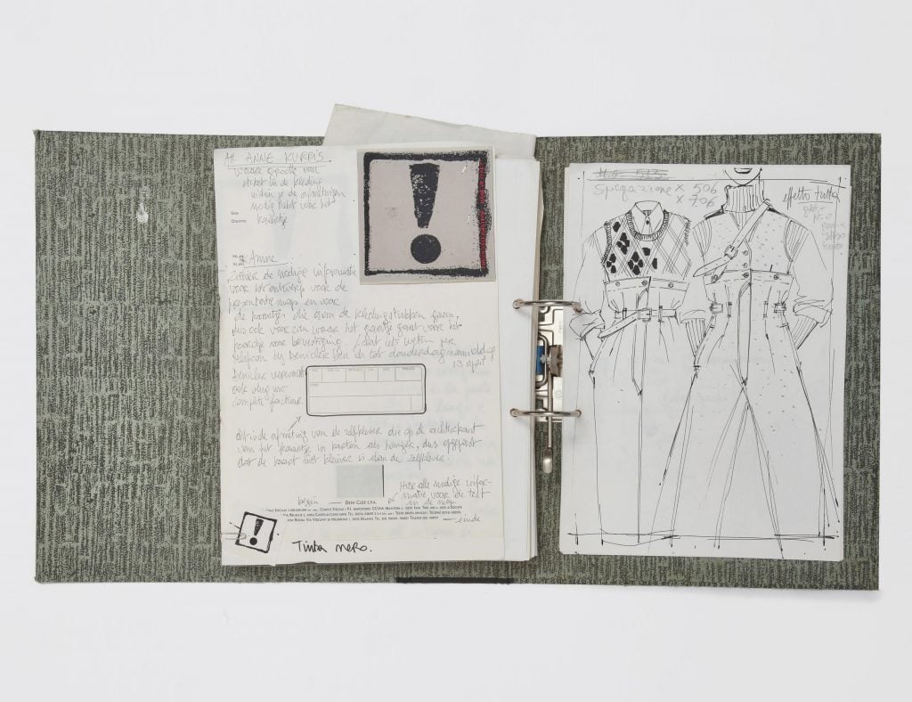 A photograph depicting an open gray patterned binder filled with fashion sketches, as seen against a white background.