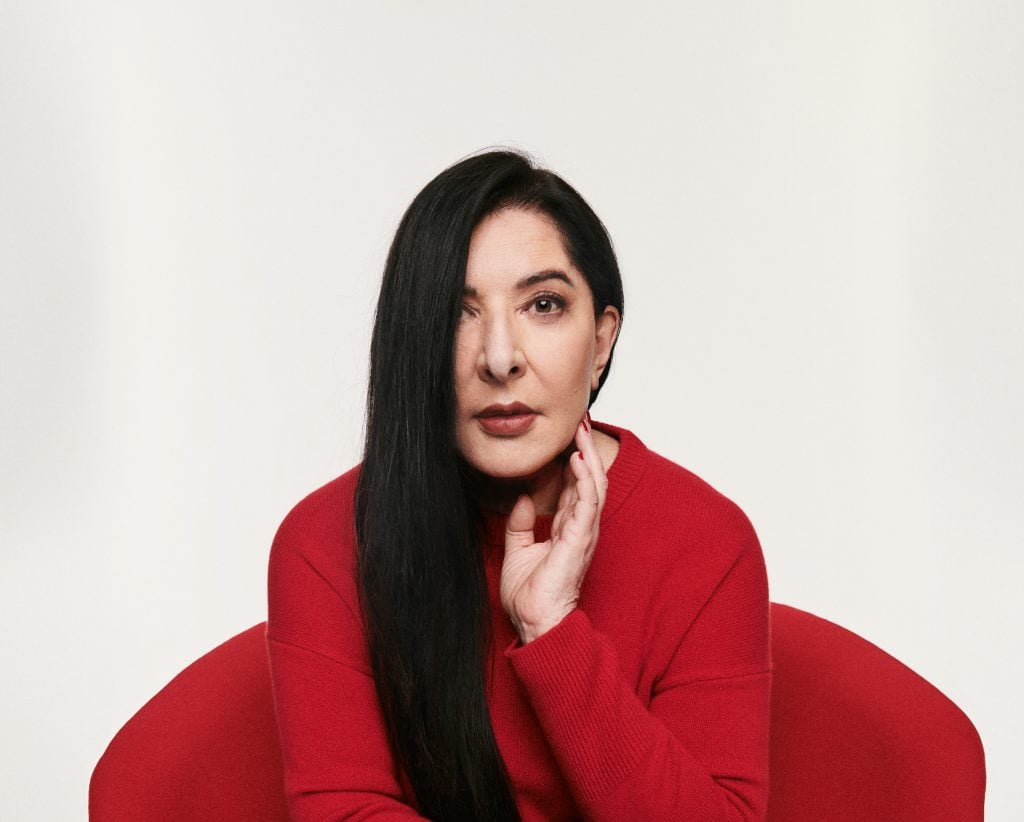 Portrait of Marina Abramović in a red top, with her long hair parted to the side