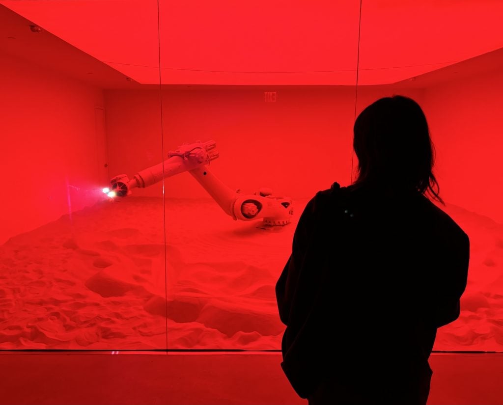 A woman looks at a robot arm in a red-lit gallery