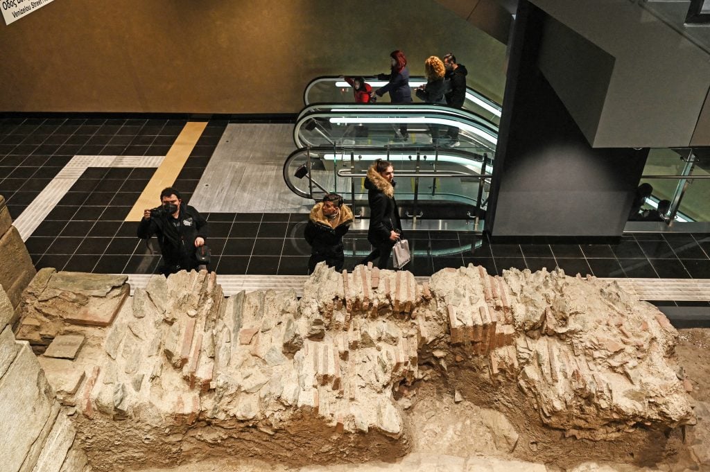 An image of people in the Greek metro surrounded by ancient ruins