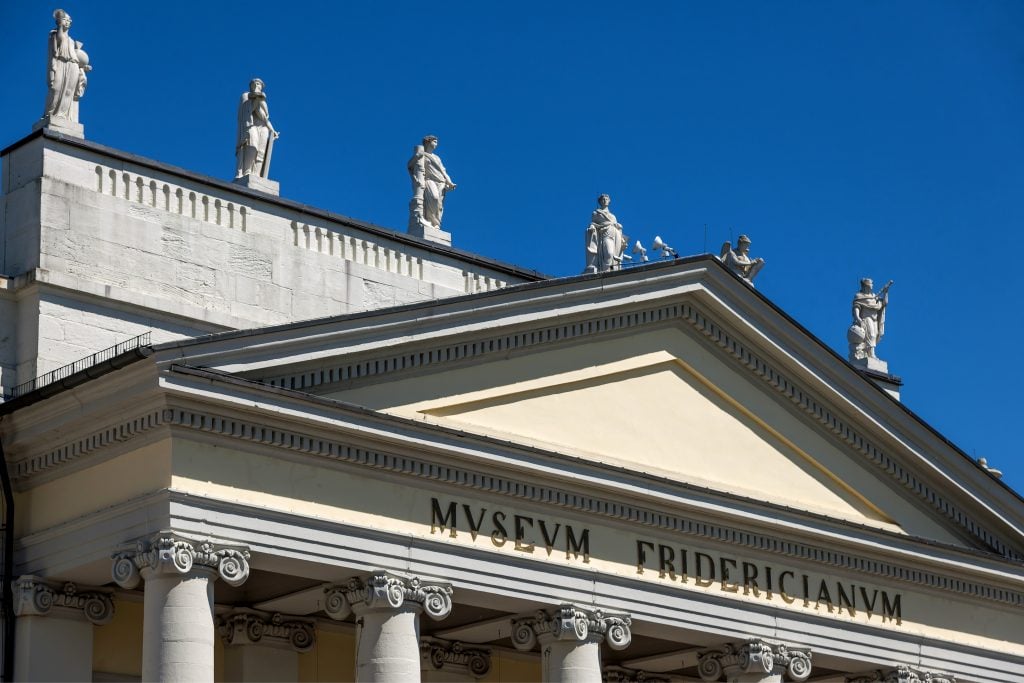 A entrance of Museum Fridericianum in Germany, showing a Classical edifice with statuettes on a parapet