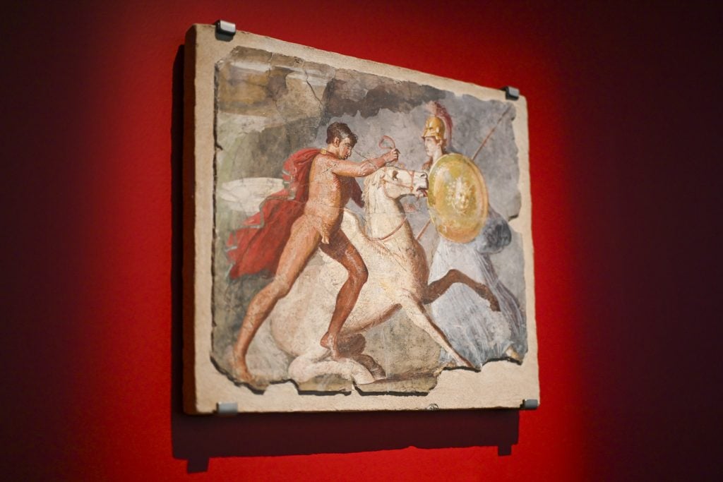 Fresco depicting a dramatic battle scene of a soldier on horseback, displayed on red walls.