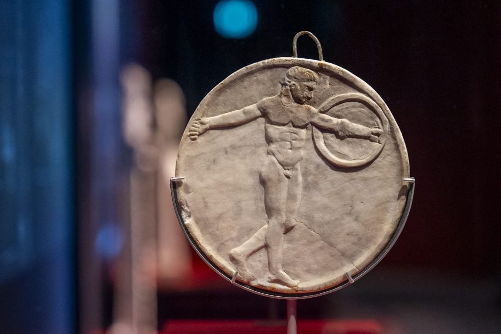 Ancient circular relief carving of a male figure holding a discus, displayed in a museum.