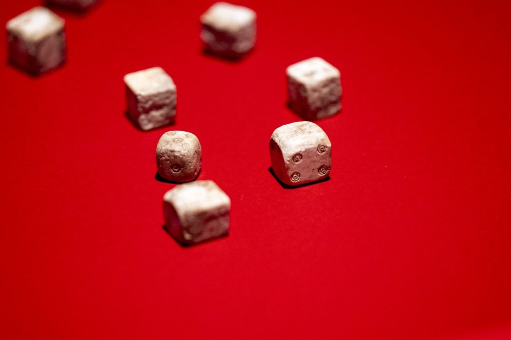 Ancient dice artifacts resting on a bold red surface, highlighting their weathered texture and details.