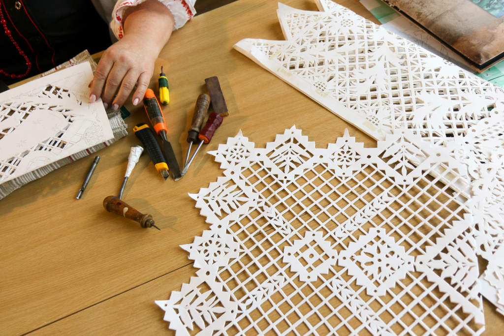 hands touch paper with decorative patterns cut into it, seen from above on a table