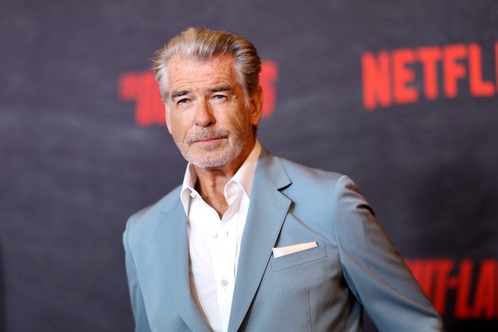 Pierce Brosnan with grey beard and in a blue suit on the red carpet