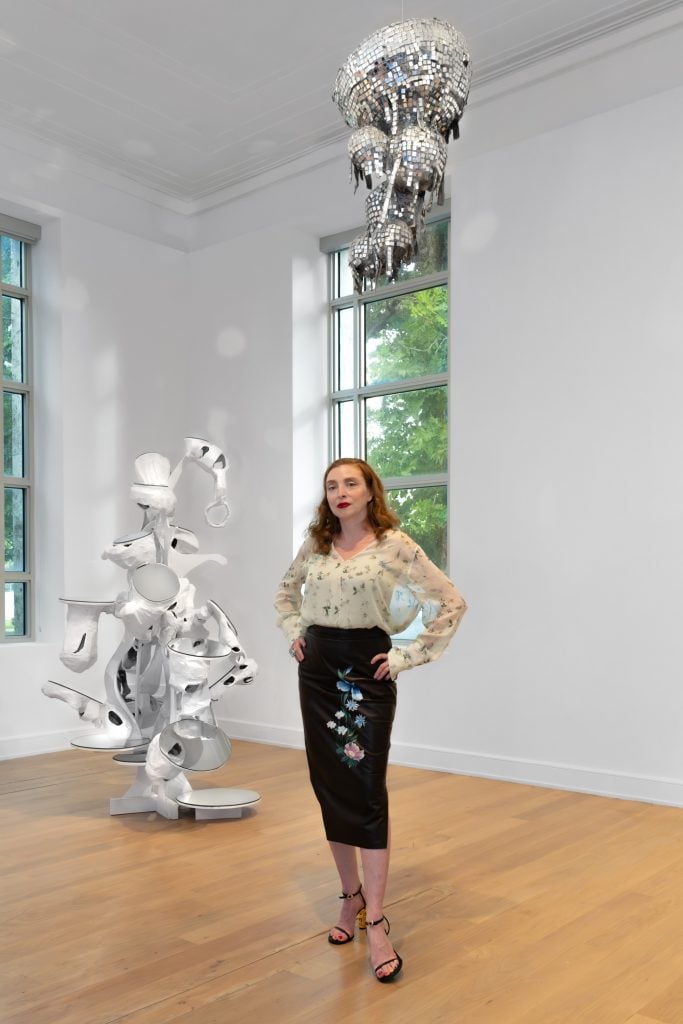 Portrait of Rachel Feinstein standing in a windowed gallery space at the Bass Museum with two of her sculptural works, image featured on the front cover of Gagosian Journal Miami 2024.