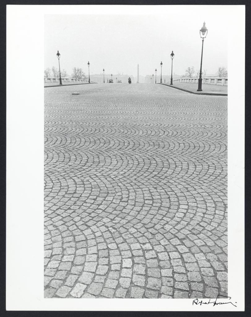 A black and white photograph depicting a cobblestone street lined with streetlamps.