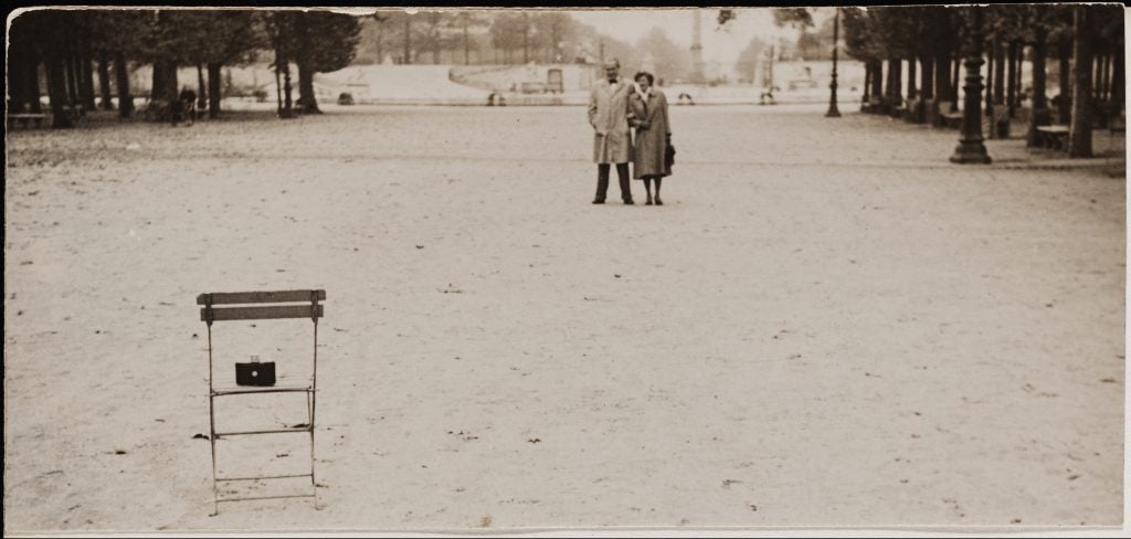 A sepia-tinged black and white photo of a couple standing far away on the other edge of a wide open public park.