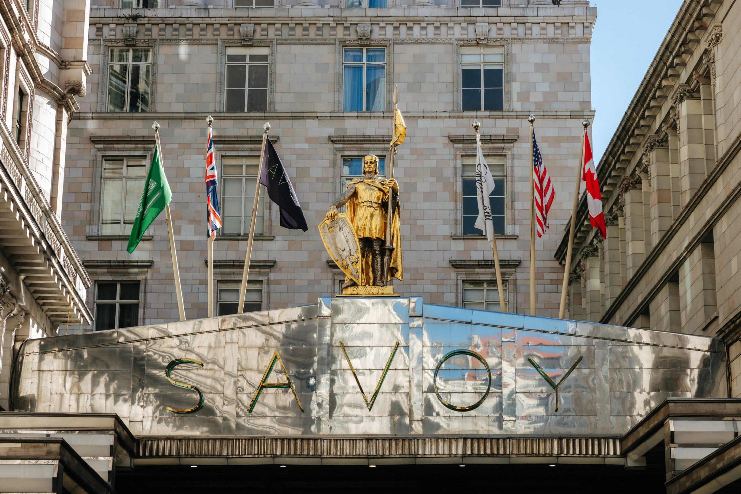 Exterior view of the iconic Savoy Hotel in London, featuring a golden statue and flags