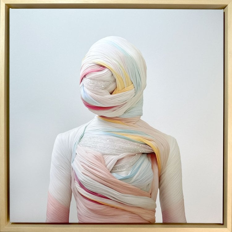 Framed artwork depicting a figure wrapped entirely in soft, pastel-colored fabric with shimmering accents, creating a serene and abstract visual effect.