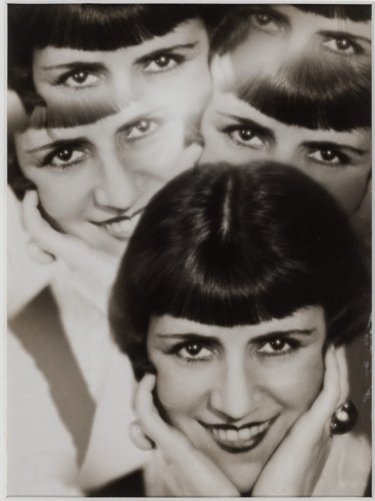 A Surrealist black and white photograph depicting a woman with a short dark bob holding her head in her hands, with four echoes of the same images emanating in two columns above her head.