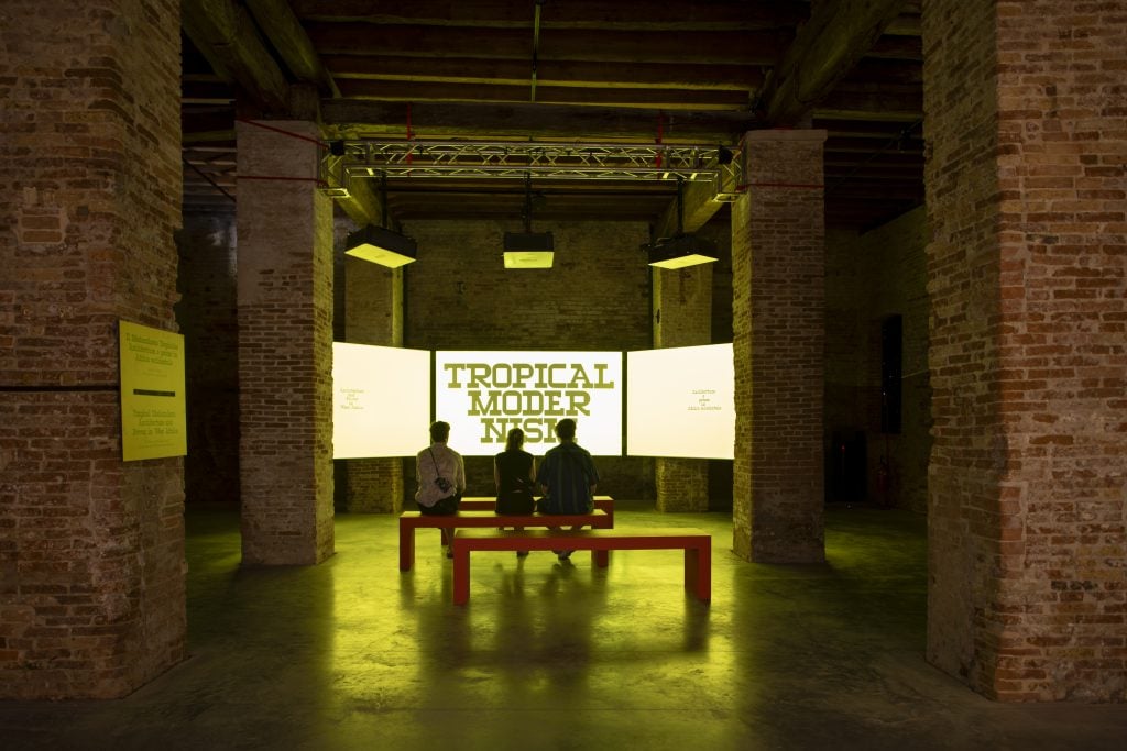 Gallery view showing three visitors sitting on a bench and watching a film