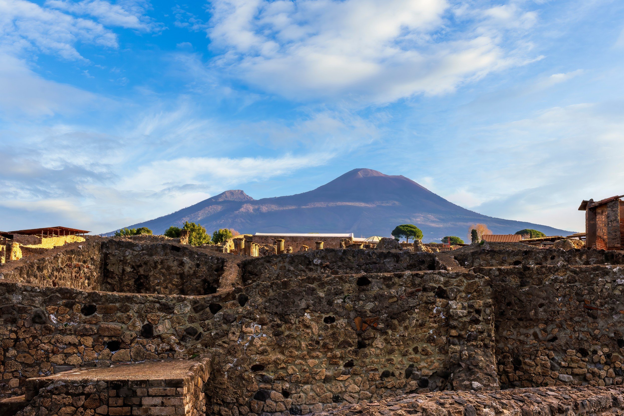 A scenic view of Pompeii ruins with Mount Vesuvius towering under a bright blue sky.