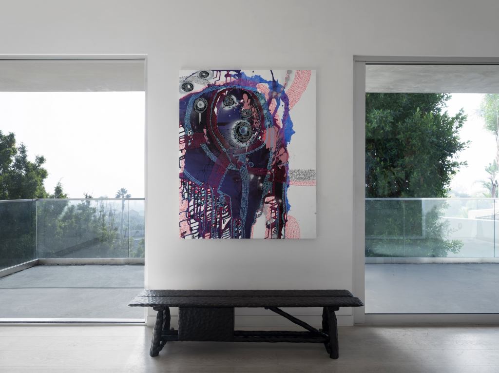 A photograph depicting a purple-tinged abstract artwork hanging on a white wall over a bench between two open doors leading out to a grey day on an LA deck.