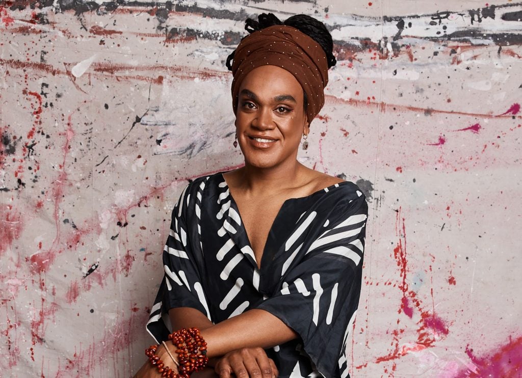 Artist Zaachariaha Fielding posing while seated in front of a canvas with red splatters