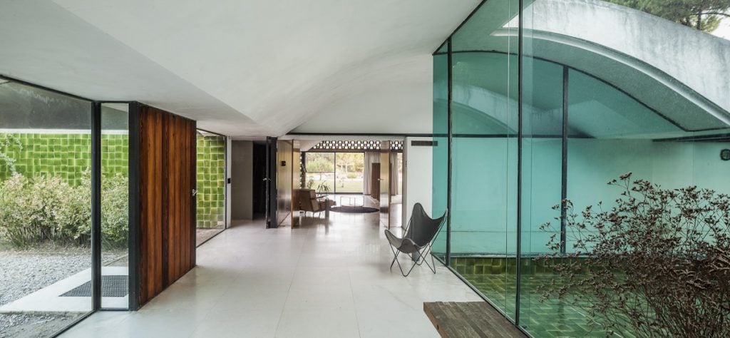 Spacious interior of Casa Gomis, featuring glass walls, green tiles, and mid-century modern decor.