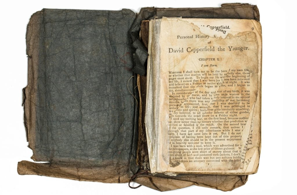 a very old and damaged looking book that is open and you can see its opened to the first page of the novel 'David Copperfield'