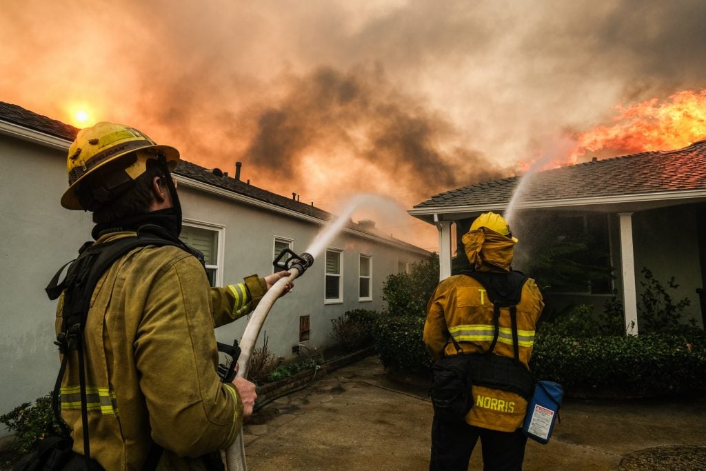 two fire fighters hose down a burning house