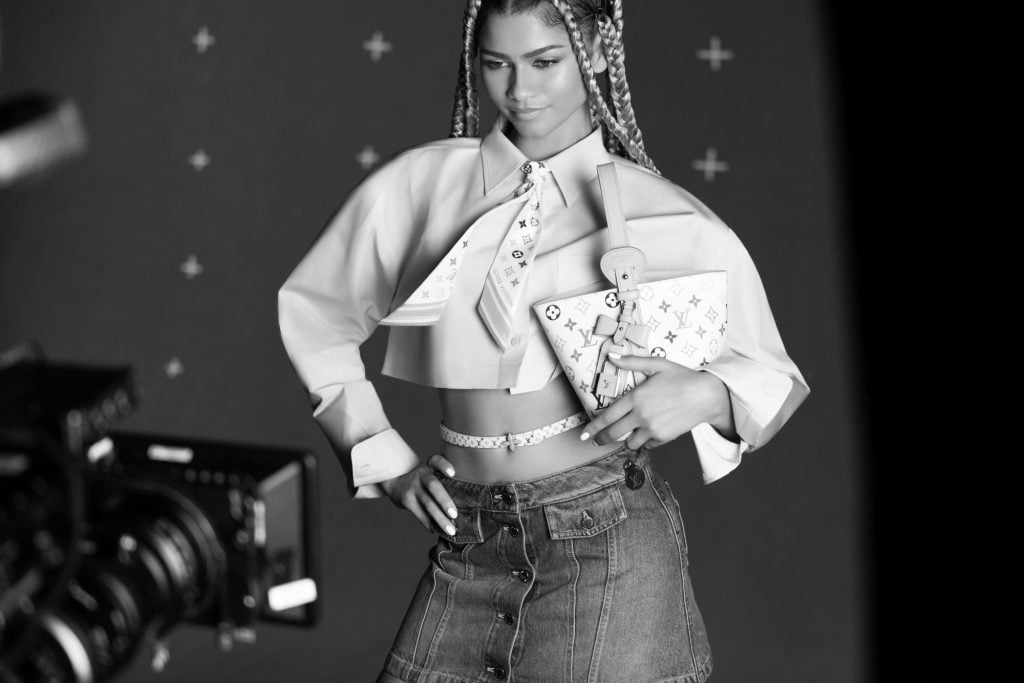 black and white photograph in which a woman wearing an outfit with many details and monograms showing it is Louis Vuitton clothes poses in front of a camera