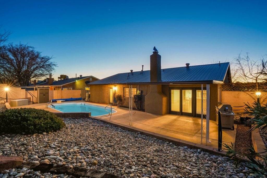 The backyard of the Breaking Bad house features a swimming pool and patio, lit during twilight.