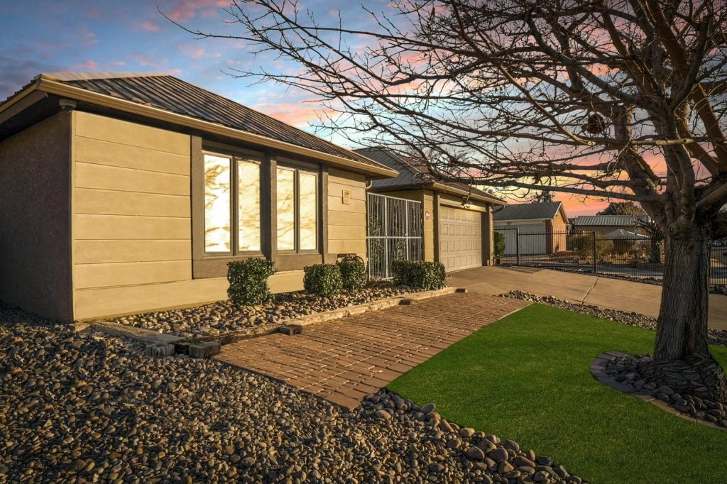 A vibrant sunset glows behind the Breaking Bad house, highlighting the tidy yard and gravel landscaping.