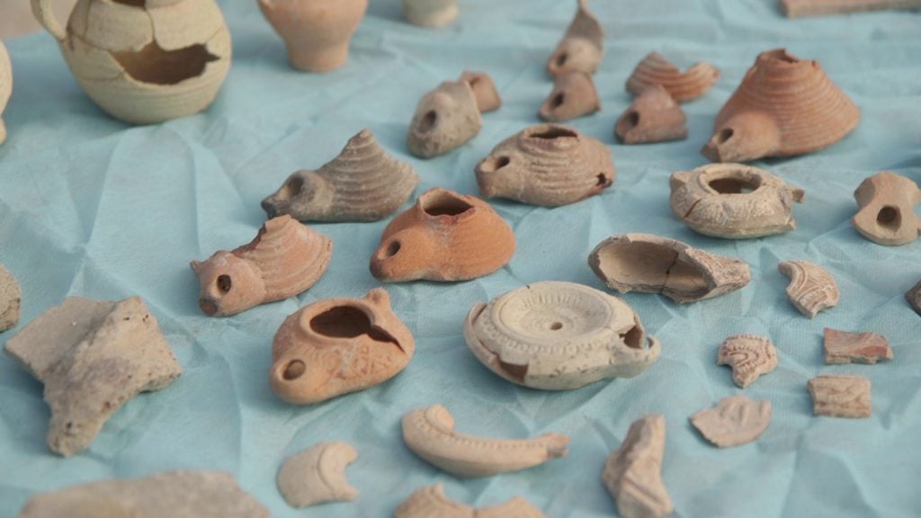 Ancient terracotta lamps and pottery fragments from a Byzantine monastery displayed on a blue cloth.