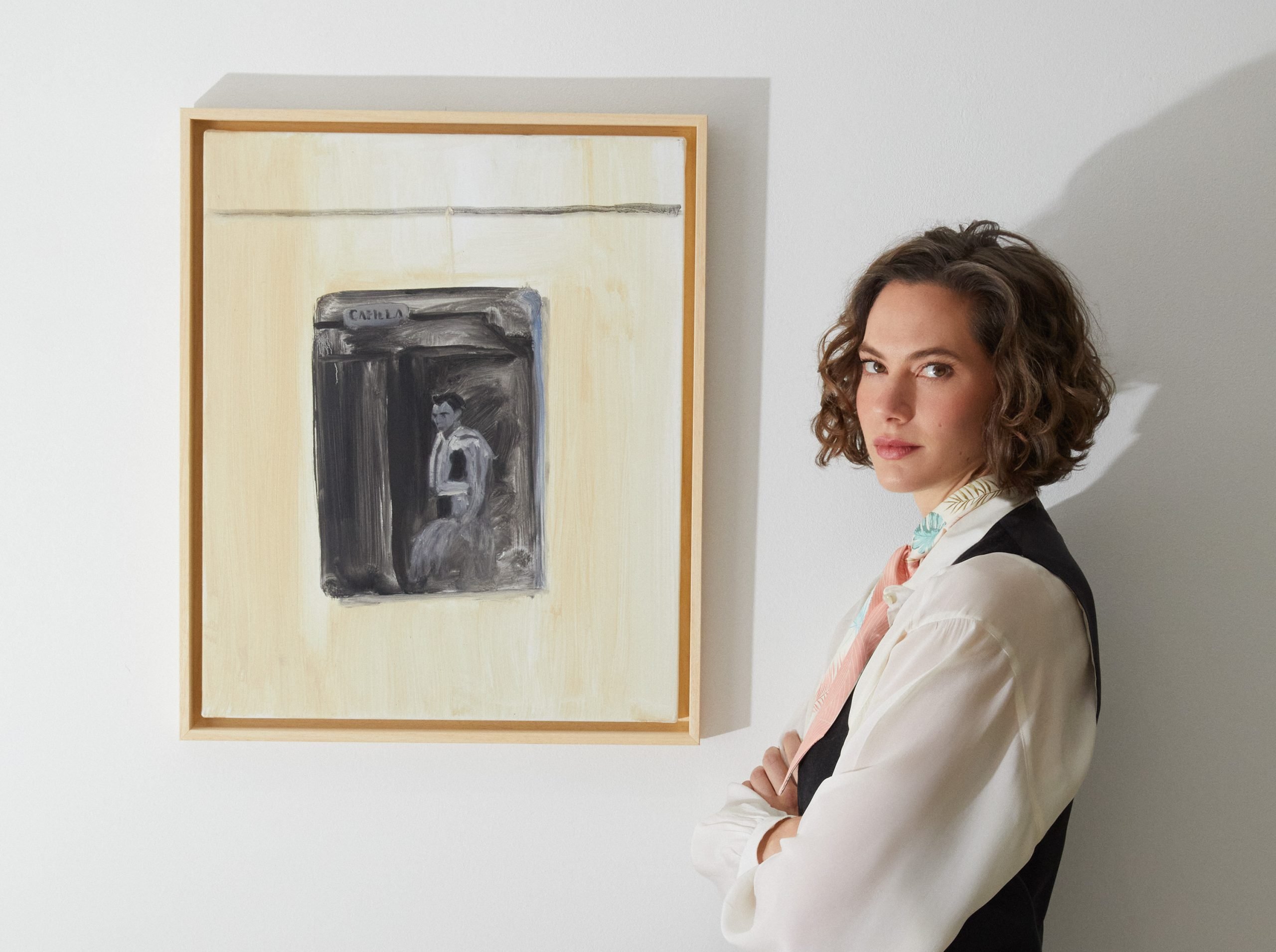 Emma Ferrer, in a white shirt and black vest, posing next to her painting of a matador