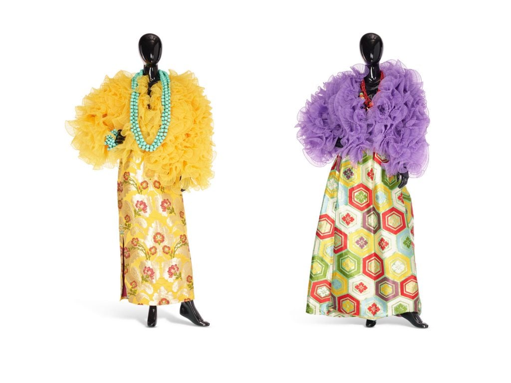 Two mannequins showcasing colorful, flounced jackets paired with bold patterned skirts and statement necklaces.