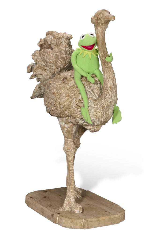 A whimsical sculpture featuring Kermit the Frog perched atop a carved ostrich with detailed feather textures.