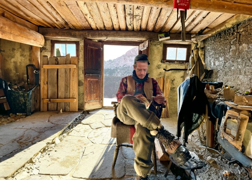 A man in winter regalia sits in a cabin