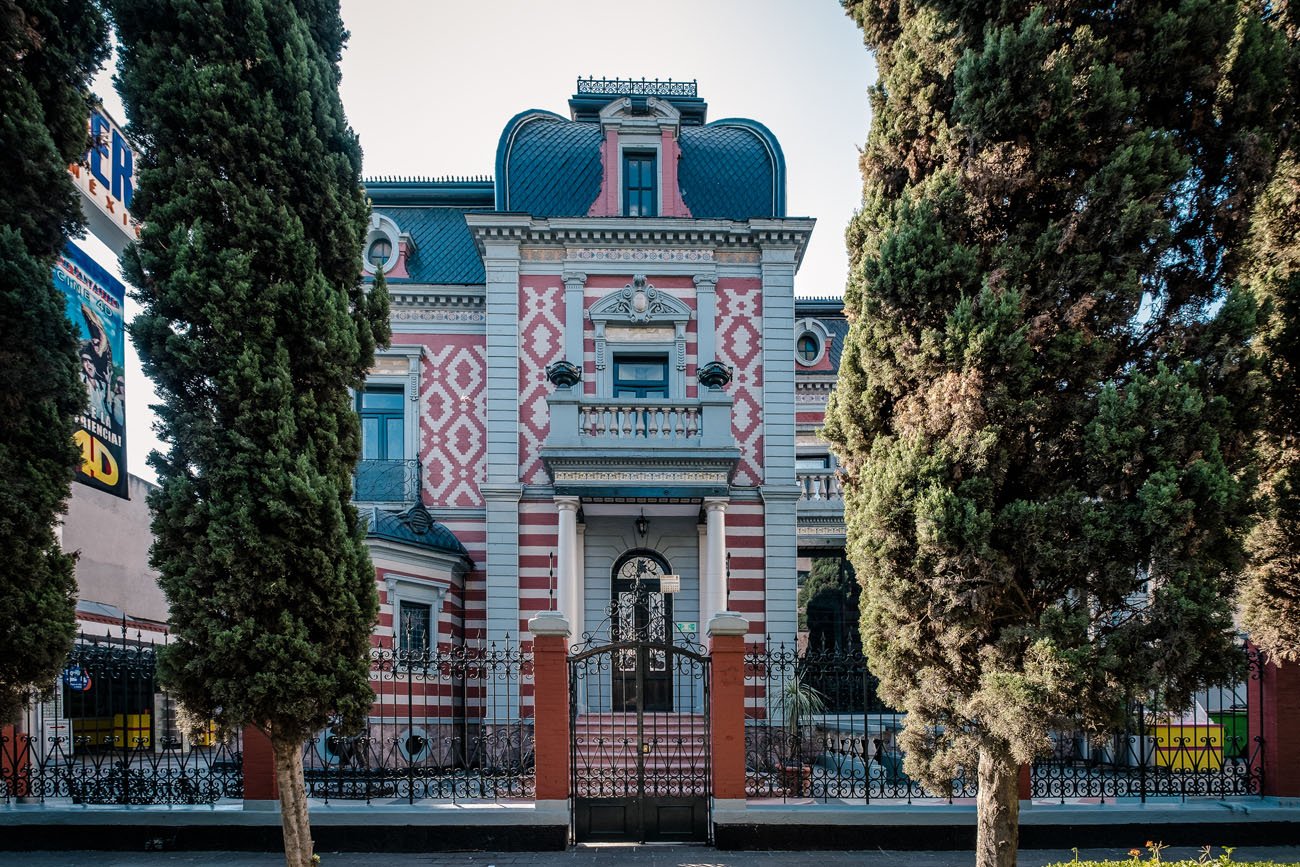 Ornate red-and-white facade of Mexico City’s Wax Museum, framed by two tall cypress trees.