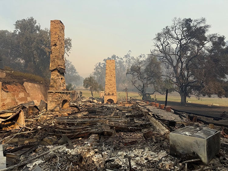 Black, burned wood on the ground, with two brick chimneys standing amid the devastation