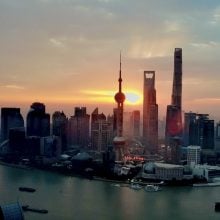 The sun rises on an epic metropolis. Large boats float in a river beside it