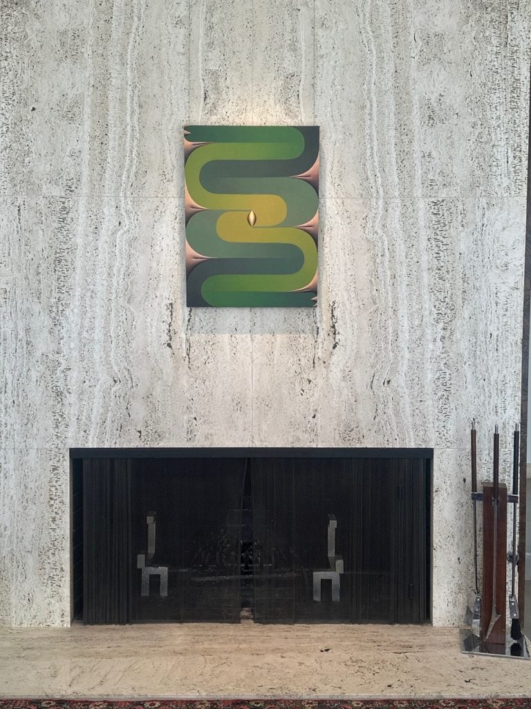 An abstract painting of green and yellow is positioned on a wall above a fireplace