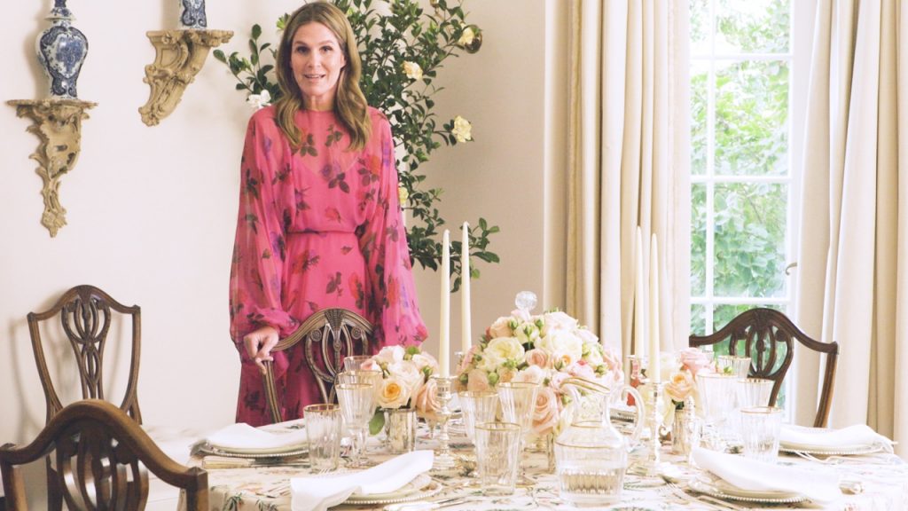 a white woman in a pink dress stands in front of a beautifully decorated table