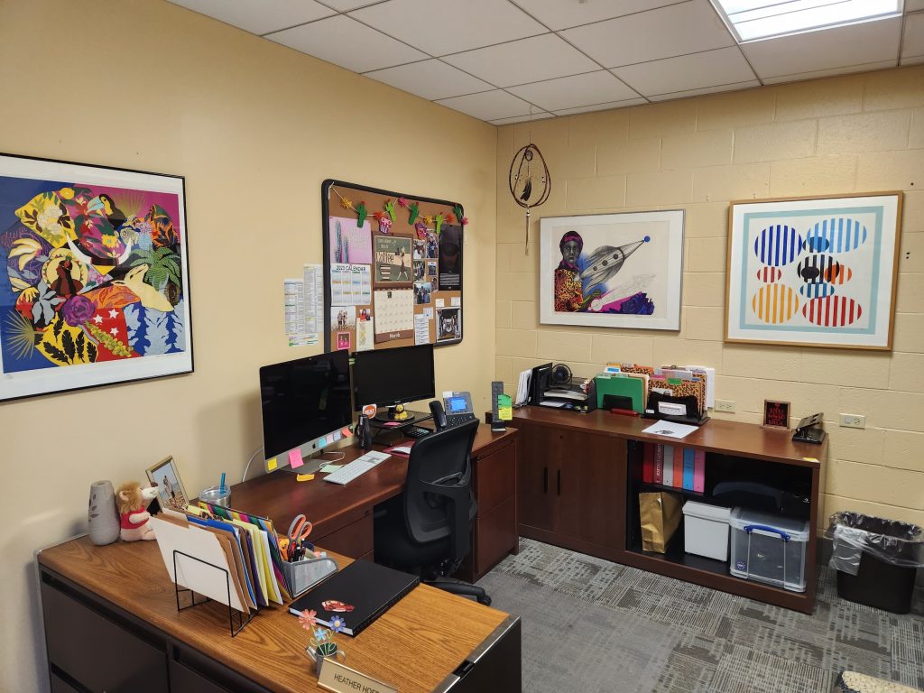 Office at Albright College featuring framed modern and contemporary artworks from the Freedman Gallery collection, with a colorful abstract painting, a portrait, and a geometric print displayed above organized desks.