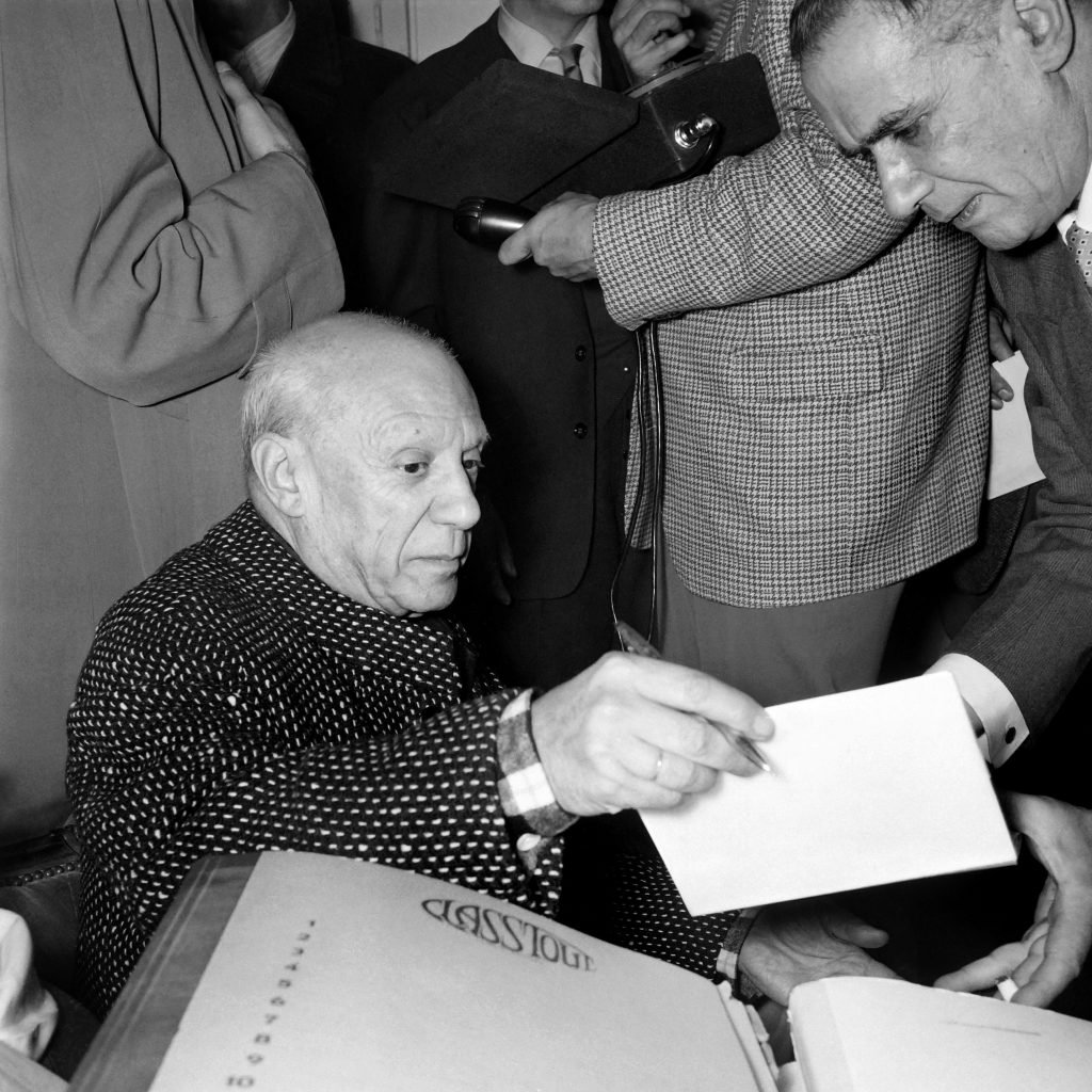 A photo shows Pablo Picasso signing autographs 