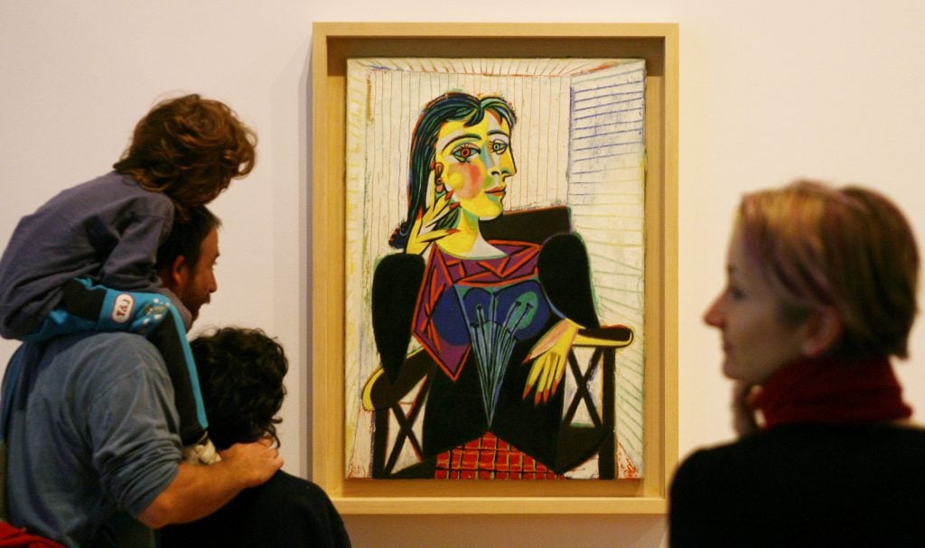 Visitors admire Picasso’s colorful cubist portrait of Dora Maar displayed in a modern art museum.