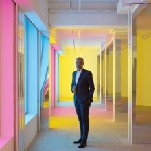 A man in a suit is pictured in a rainbow-lit chamber