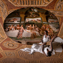 a woman in a white dress stares into a mirror reflecting magnificent frescoed walls, it is a circular mirror placed on a grand mosaiced floor