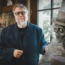 Guillermo del Toro standing beside a skeletal figure in a top hat inside his Bleak House collection.