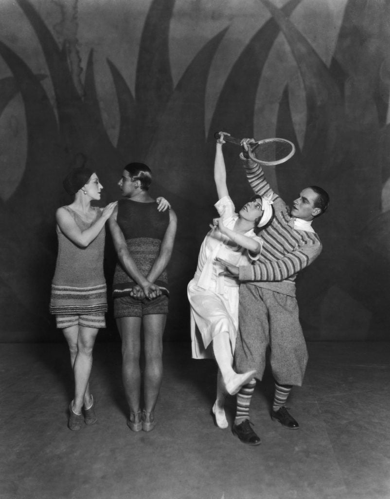 Black-and-white photo of four Ballets Russes dancers performing Le Train Bleu, with two in swimwear and two in tennis outfits striking stylized poses on stage.